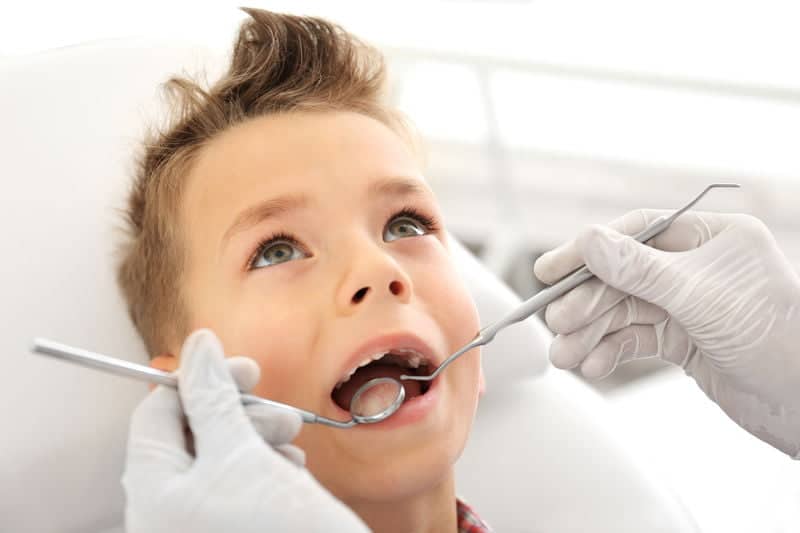 רופא שיניים בודק את שיני הילד טיפול שיניים לילד